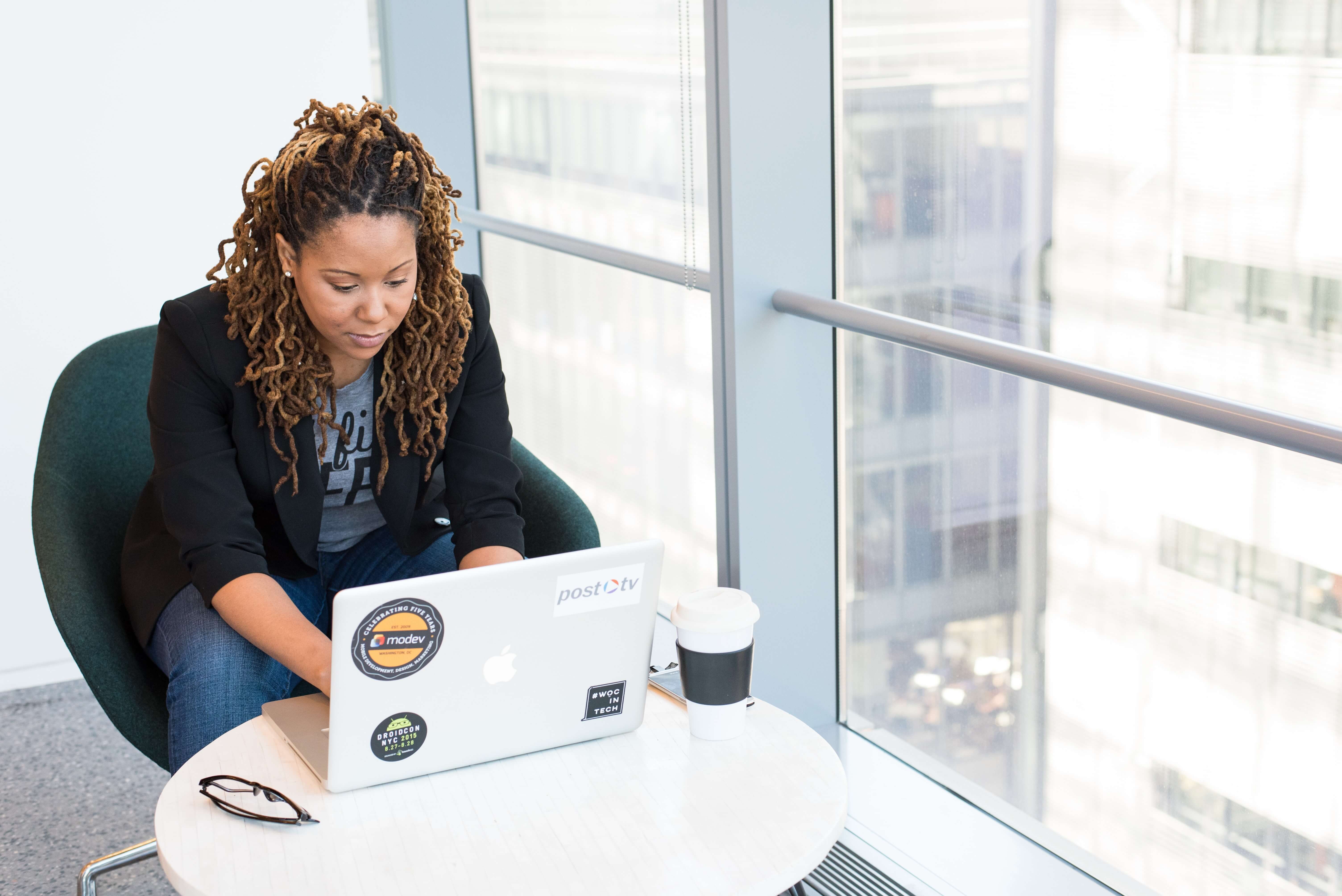 Black woman sits on laptop in clean and bright office environment.